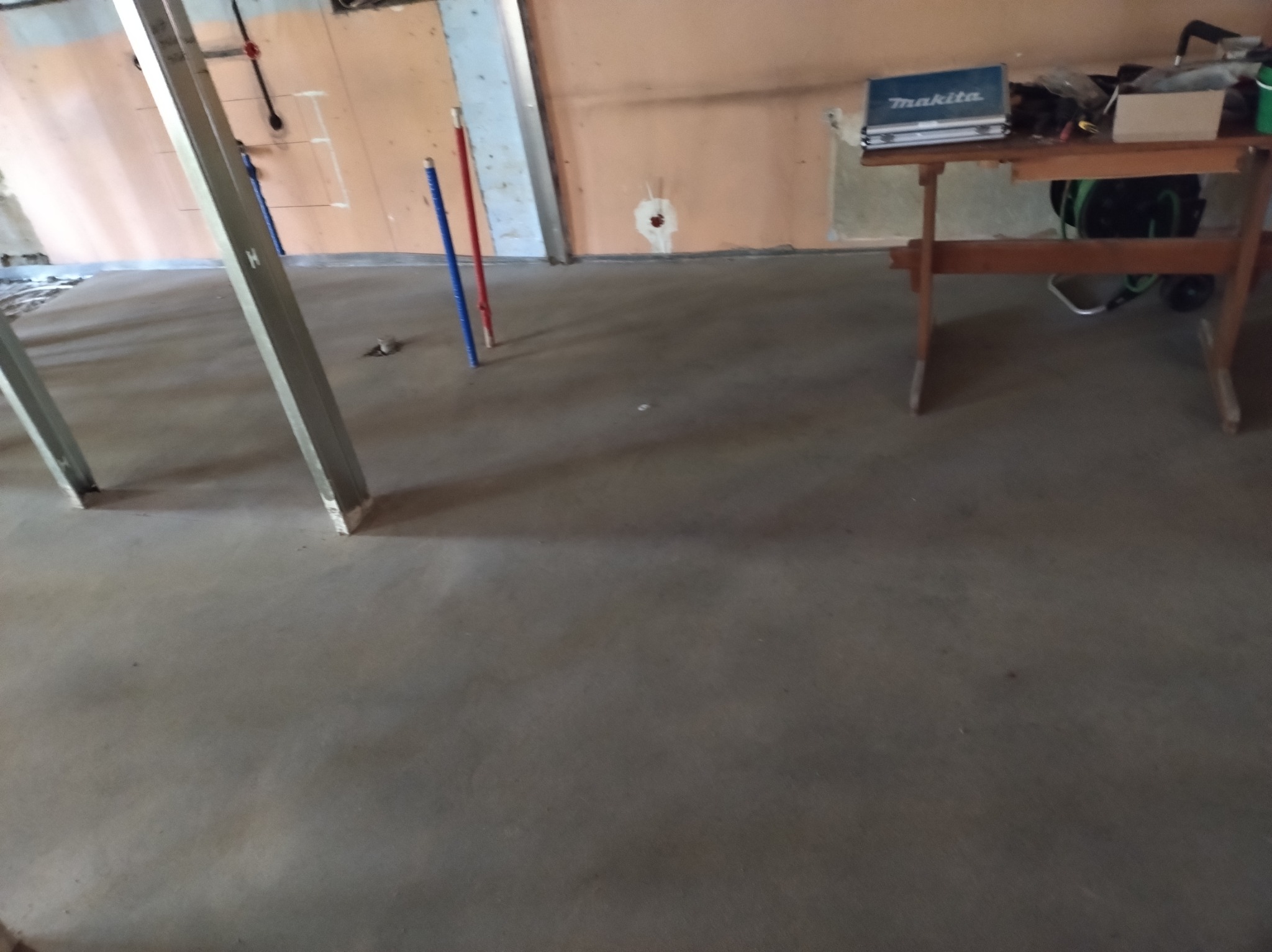 Wylana, świeża posadzka w remontowanym mieszkaniu. Widoczne profile, rurki i narzędzia Makita na stole. Ściany w trakcie wykończenia.