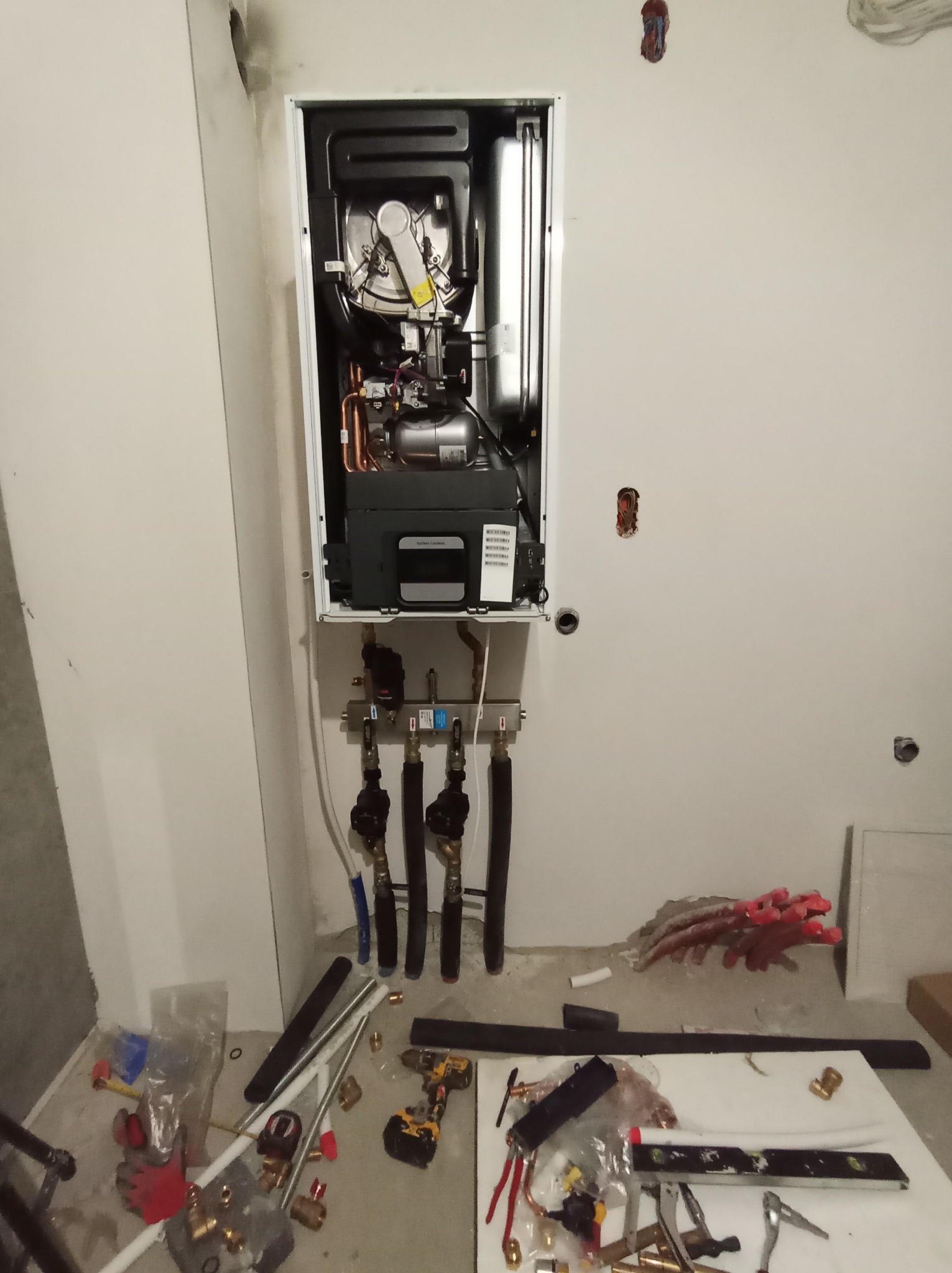 Nowy, wiszący piec gazowy z podłączonymi rurami instalacji CO, zamontowany na ścianie w surowym wnętrzu. Na podłodze narzędzia i elementy instalacyjne.