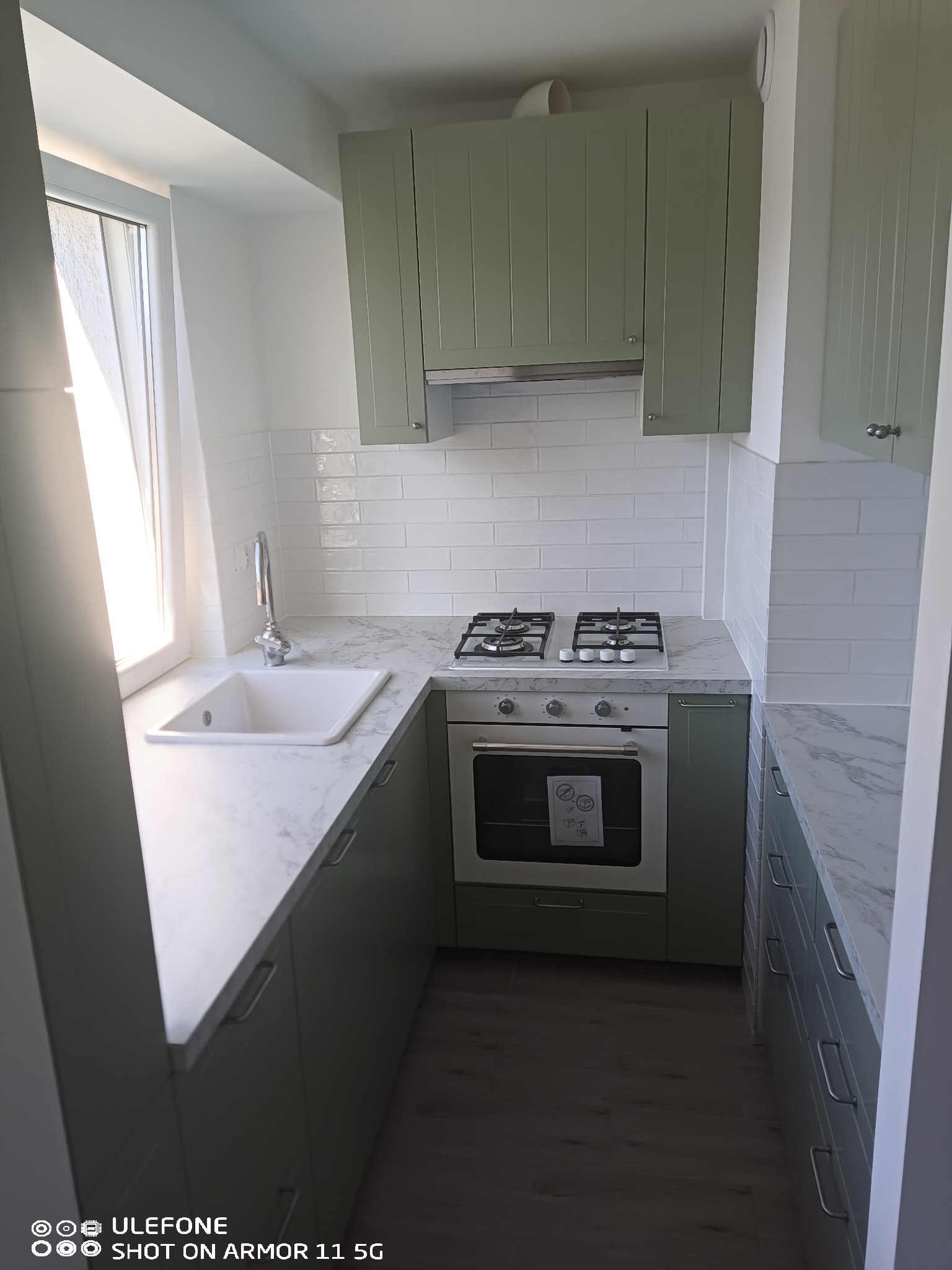 Jasna kuchnia po remoncie: pistacjowe szafki z frezowanymi frontami, białe płytki metro i marmurowy blat. Nowoczesny design z elementami retro.