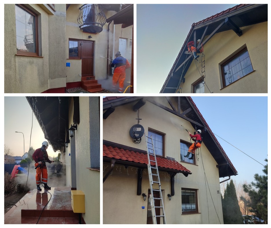 Pracownik w pomarańczowym kombinezonie, zabezpieczony linami, myje elewację domu jednorodzinnego pod wysokim ciśnieniem; widoczna drabina, antena satelitarna i okna z brązowymi ramami.
