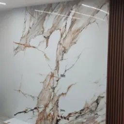 Wykończenie ściany w Łomży z użyciem płyty imitującej marmur, z widocznymi gniazdkami elektrycznymi i drewnianymi panelami dekoracyjnymi po prawej stronie, podłoga zabezpieczona kartonem.