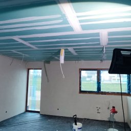 RENOWEJT Przemysław Saniewski - Wnętrze w trakcie prac wykończeniowych: sufit z płyt kartonowo-gipsowych z widocznymi łączeniami, przygotowany do dalszej obróbki, ściany po szpachlowaniu, podłoga zabezpieczona folią, na środku...