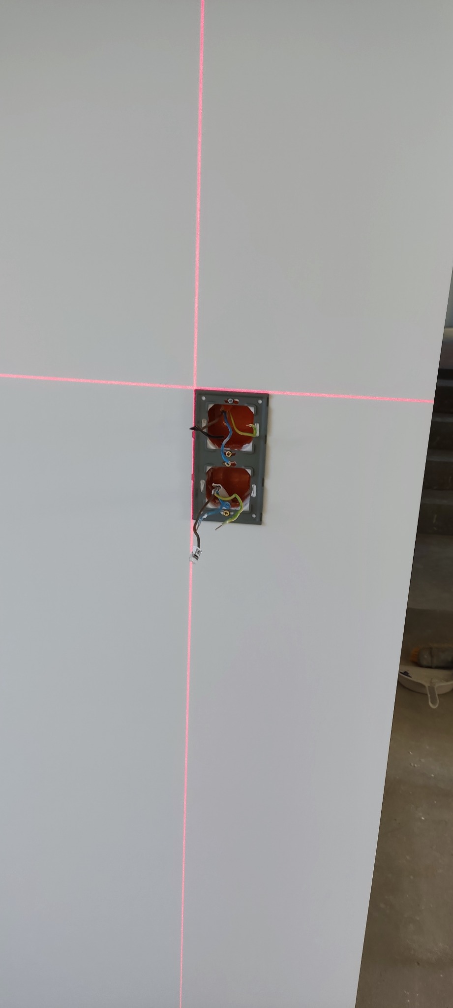 Ściana z wyznaczonym laserowo miejscem na gniazdka elektryczne, widoczne wystające przewody.