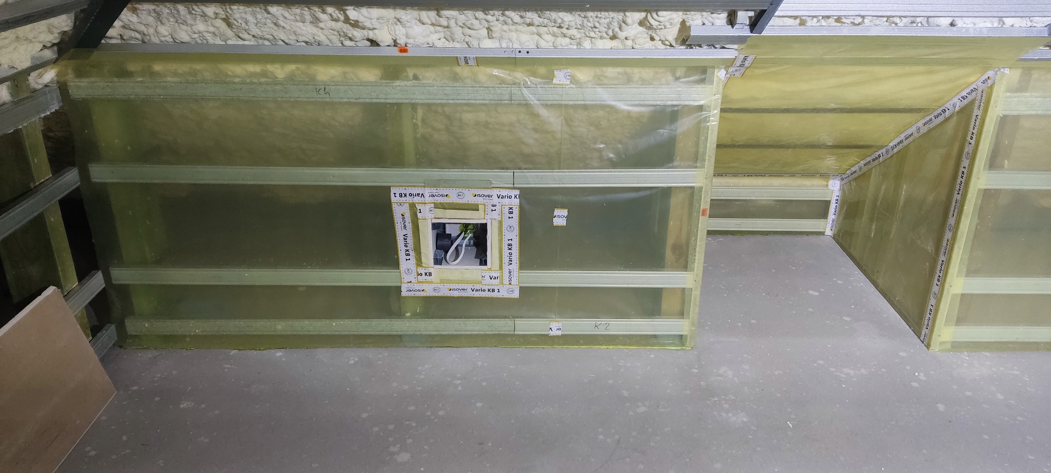 Montaż folii paroizolacyjnej na poddaszu, widoczne profile metalowe, wełna mineralna i taśma uszczelniająca wokół puszki elektrycznej.