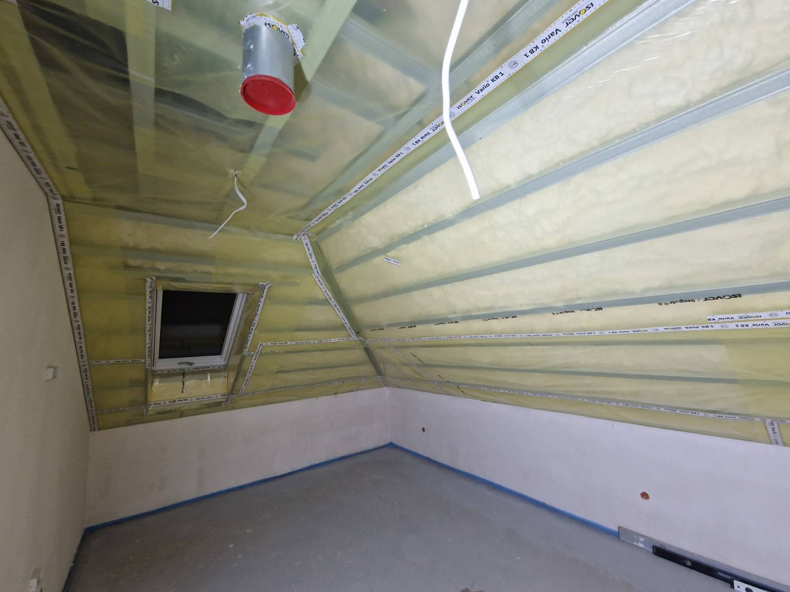 Poddasze w trakcie ocieplania, widoczne wełna mineralna, folia paroizolacyjna, profile montażowe, okno dachowe i taśma uszczelniająca na ścianach.