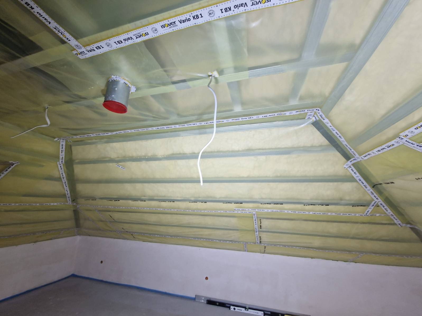 Poddasze w trakcie ocieplania wełną mineralną, zabezpieczone folią paroizolacyjną Isover Vario KB1 z widoczną metalową konstrukcją nośną i elementami instalacji elektrycznej.