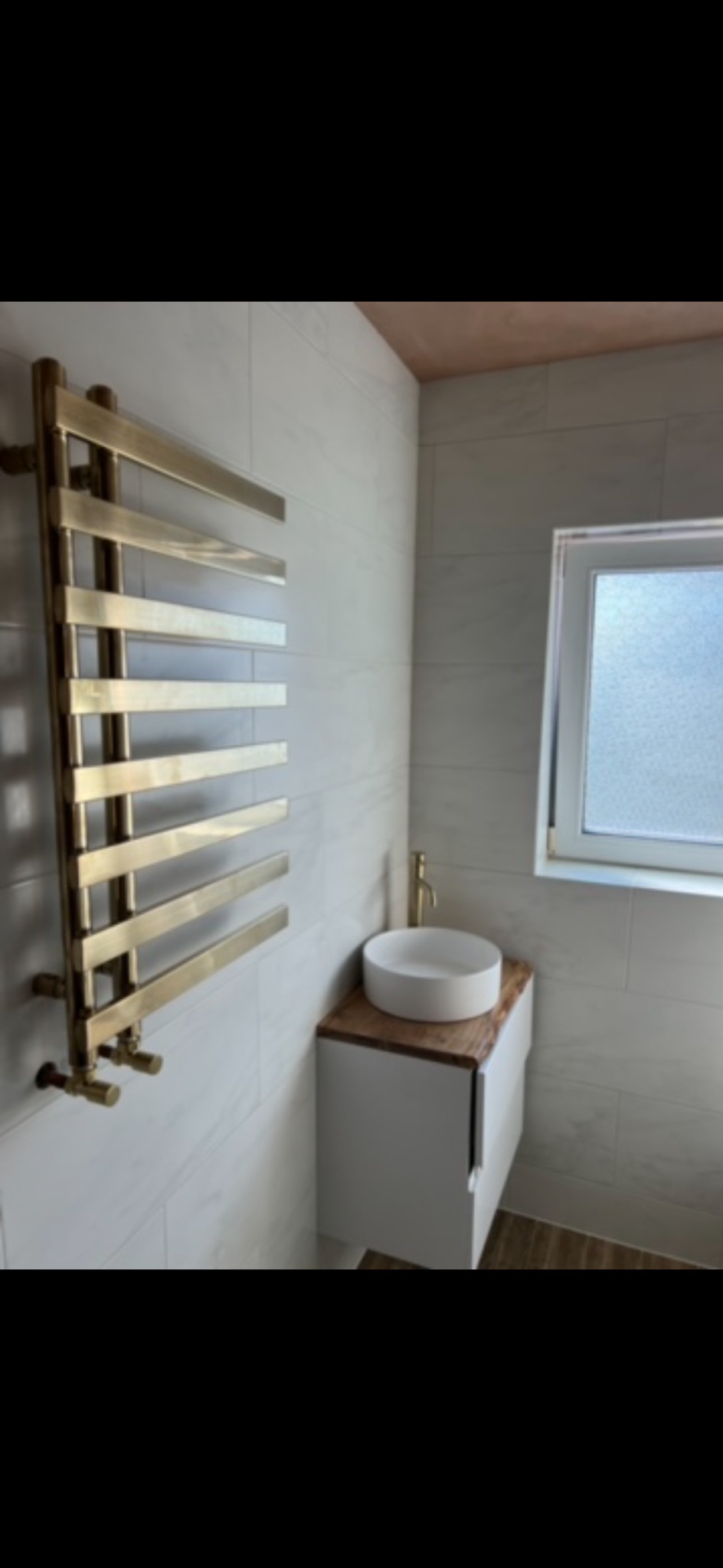 Nowoczesna łazienka z grzejnikiem drabinkowym w kolorze złotym, umywalką nablatową i białymi płytkami imitującymi marmur. Minimalistyczny design, jasne wnętrze.