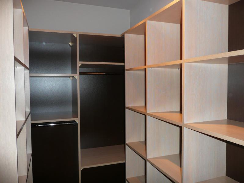 Wnętrze garderoby na wymiar z półkami w jasnym drewnie i ciemnymi panelami bocznymi, widoczny drążek na ubrania.