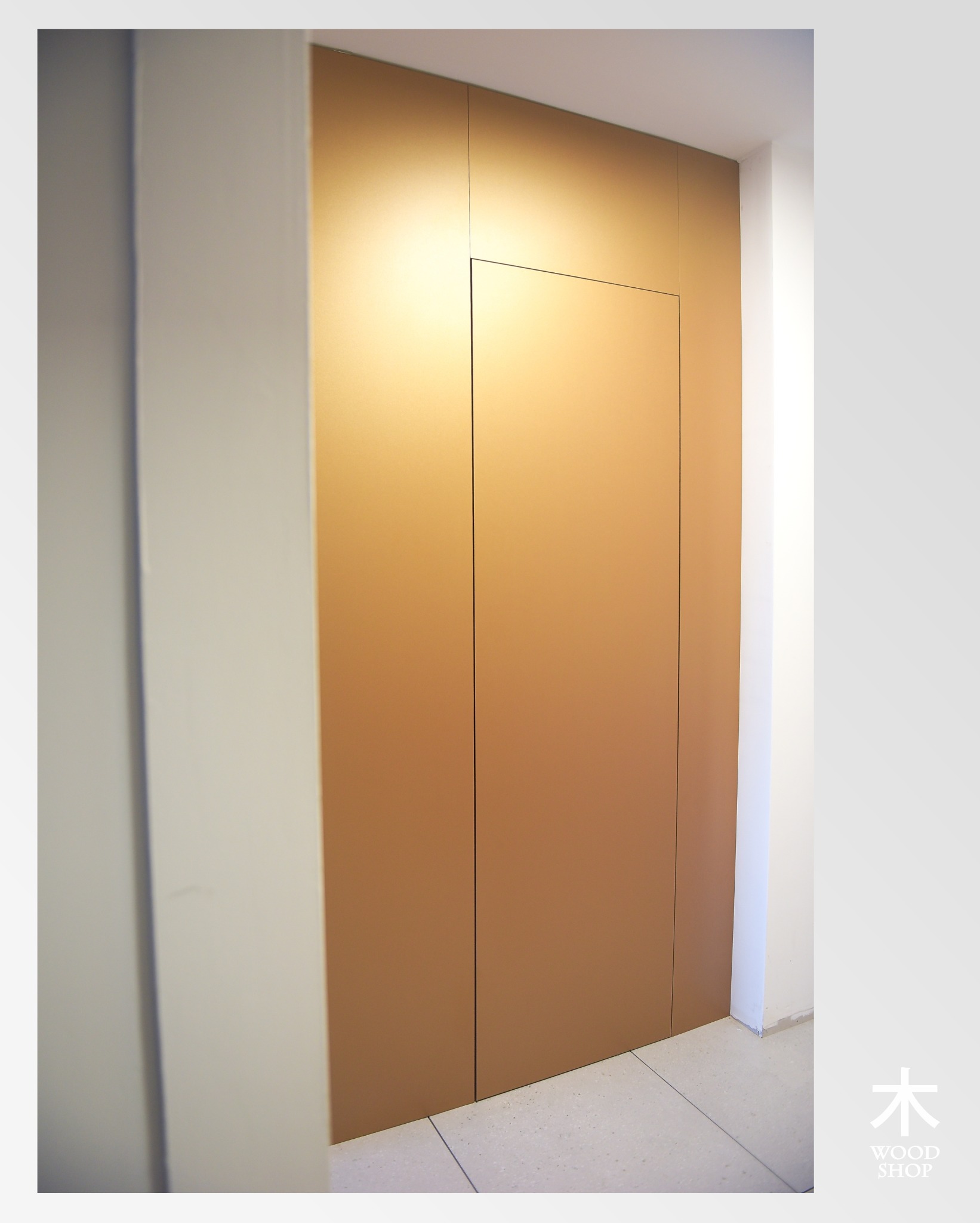 Minimalistyczna szafa wnękowa z ukrytymi drzwiami w kolorze ciepłego brązu, idealnie wkomponowana w białą ścianę. Podświetlenie górne podkreśla gładką powierzchnię.