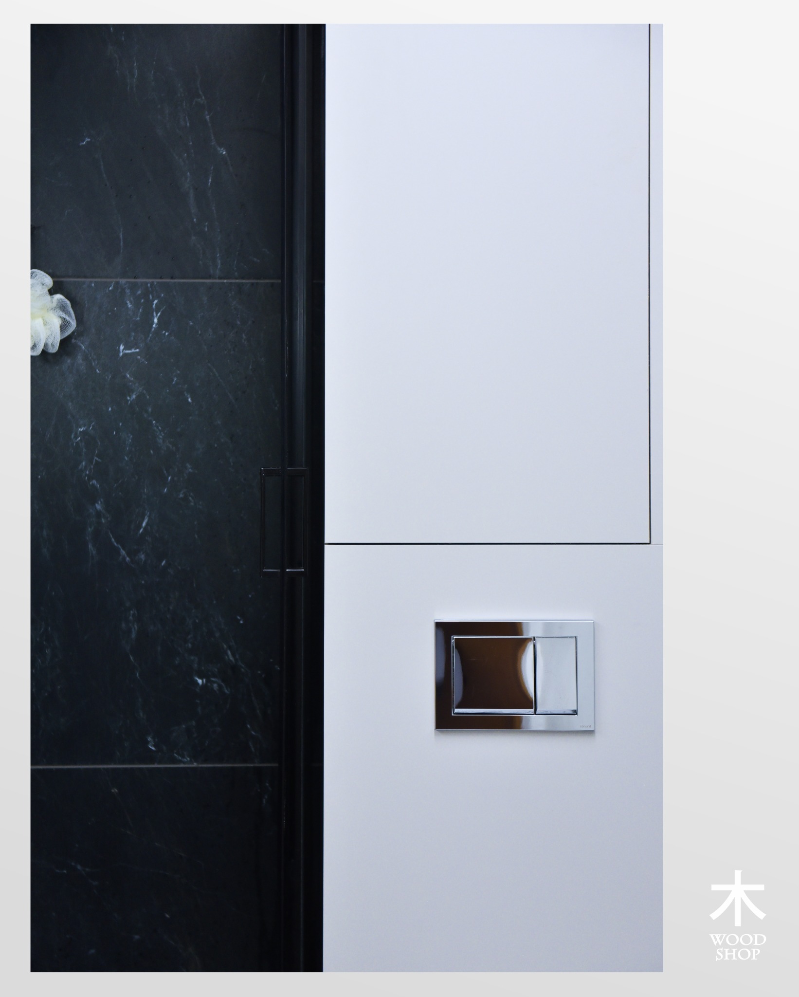 Minimalistyczna łazienka: biała szafka z chromowanym przyciskiem spłuczki, kontrastująca z czarną ścianą z marmurowym wzorem i delikatną myjką.