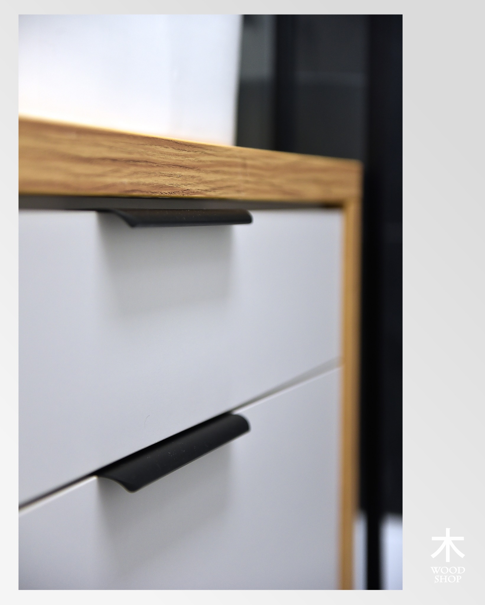 Białe szuflady z czarnymi, minimalistycznymi uchwytami i drewnianym blatem w ciepłym odcieniu. Ujęcie z bliska akcentuje detale wykończenia.