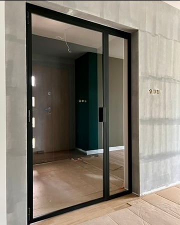 Nowoczesne przesuwne drzwi z czarną ramą, widok na wnętrze z zieloną ścianą i zabezpieczoną podłogą podczas remontu.