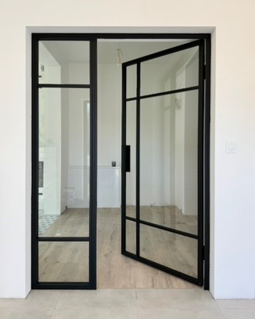 Nowoczesne, czarne drzwi szklane z metalowymi szprosami, otwarte do wewnątrz, widok na jasne wnętrze z drewnianą podłogą.