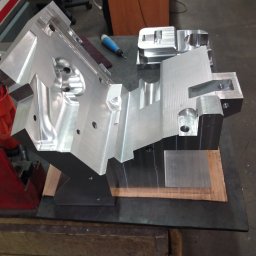 Skraw-Lech Agnieszka Lechoszest - Precyzyjnie obrobiony, srebrny blok metalu z licznymi otworami i frezowaniami, leżący na stole w warsztacie. Widoczne narzędzia i elementy obrabiane w tle.