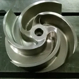 Precyzyjnie obrobiony metalowy wirnik pompy z widocznymi śladami frezowania, leżący na stole warsztatowym. Detal z bliska, oświetlenie neutralne.