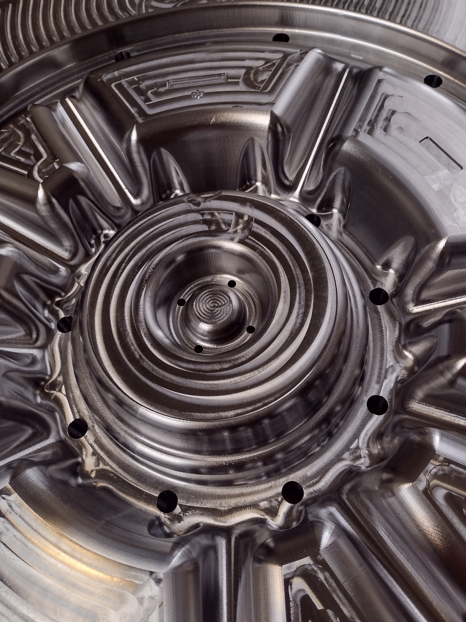 Metalowy element po obróbce CNC z widocznymi śladami frezowania i otworami, ukazujący skomplikowany, spiralny wzór. Precyzyjna obróbka z bliska.