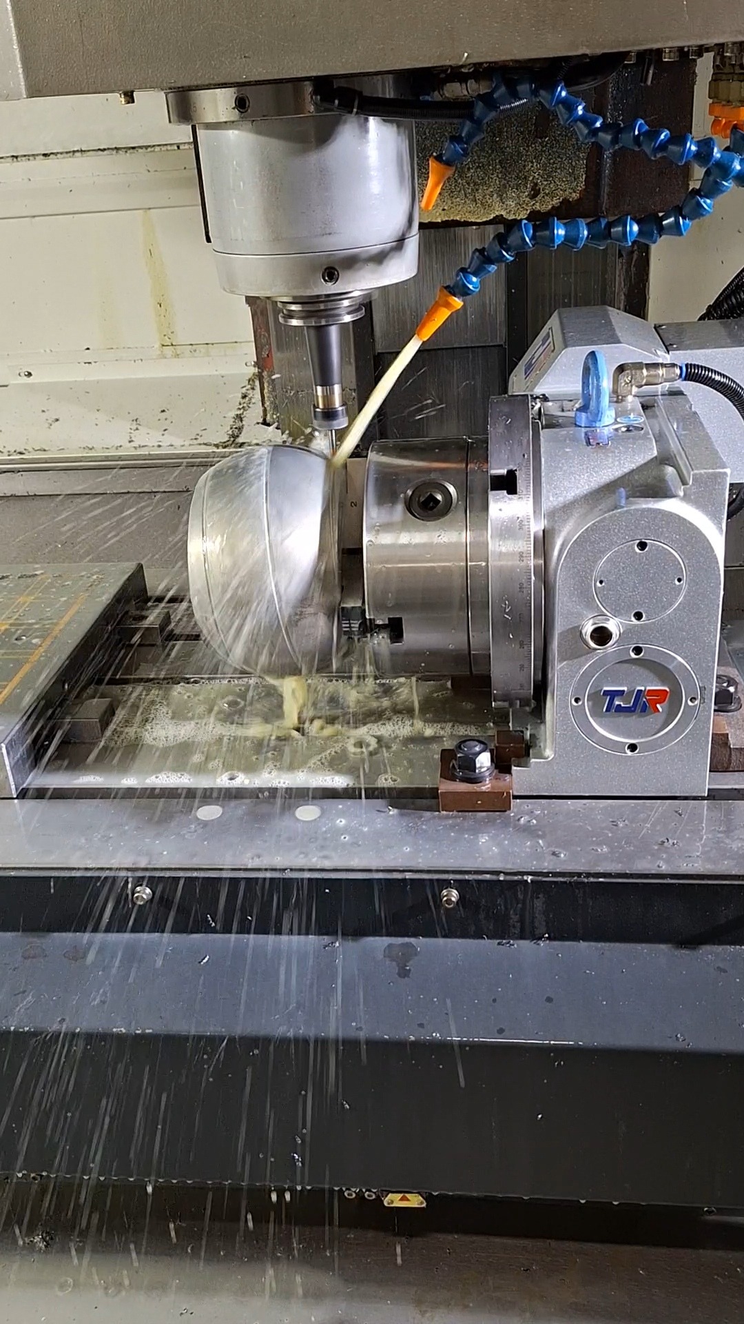 Srebrny element obrabiany w tokarce CNC z użyciem chłodziwa, widoczne wióry i narzędzie skrawające w zbliżeniu. Obróbka metalu na maszynie numerycznej.