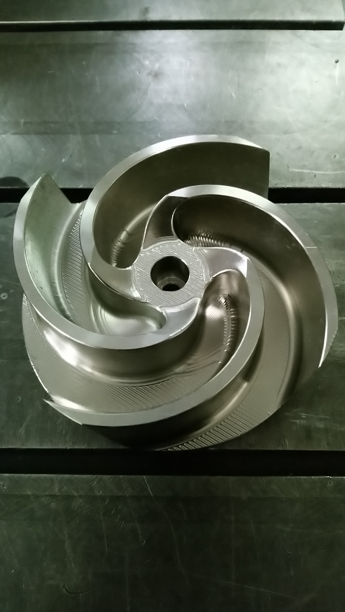 Precyzyjnie obrobiony metalowy wirnik pompy z widocznymi śladami frezowania, leżący na stole warsztatowym. Detal z bliska, oświetlenie neutralne.