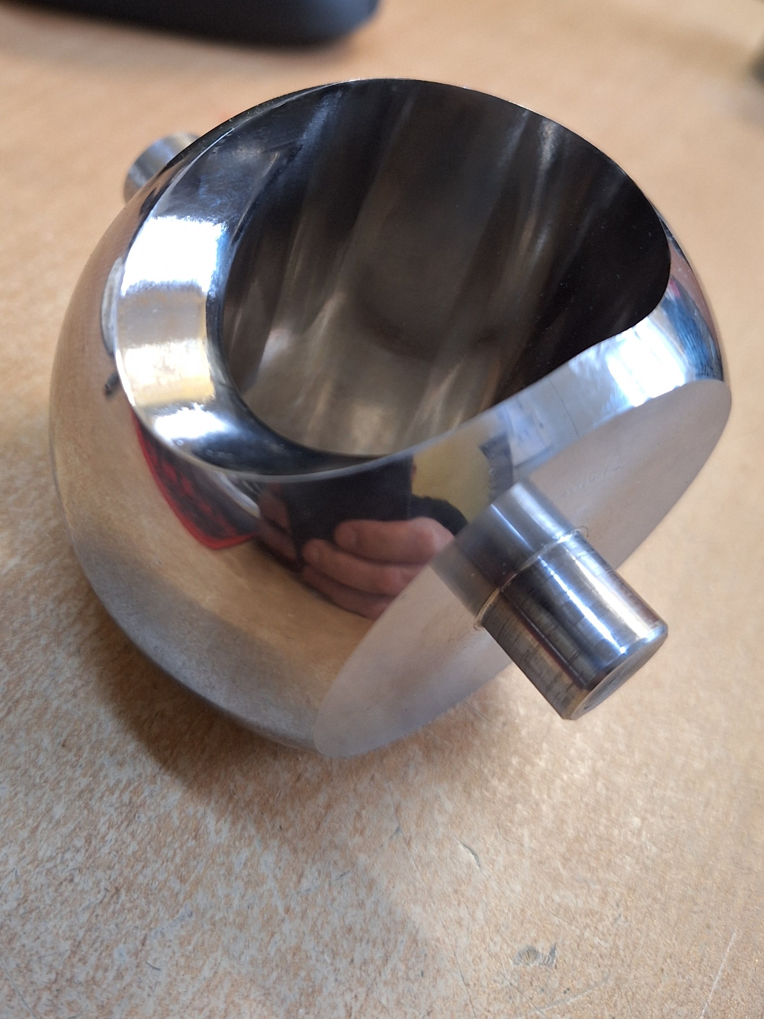 Precyzyjnie wykonany, metalowy element o kulistym kształcie z otworem i wystającym cylindrycznym uchwytem, wykończony na wysoki połysk.