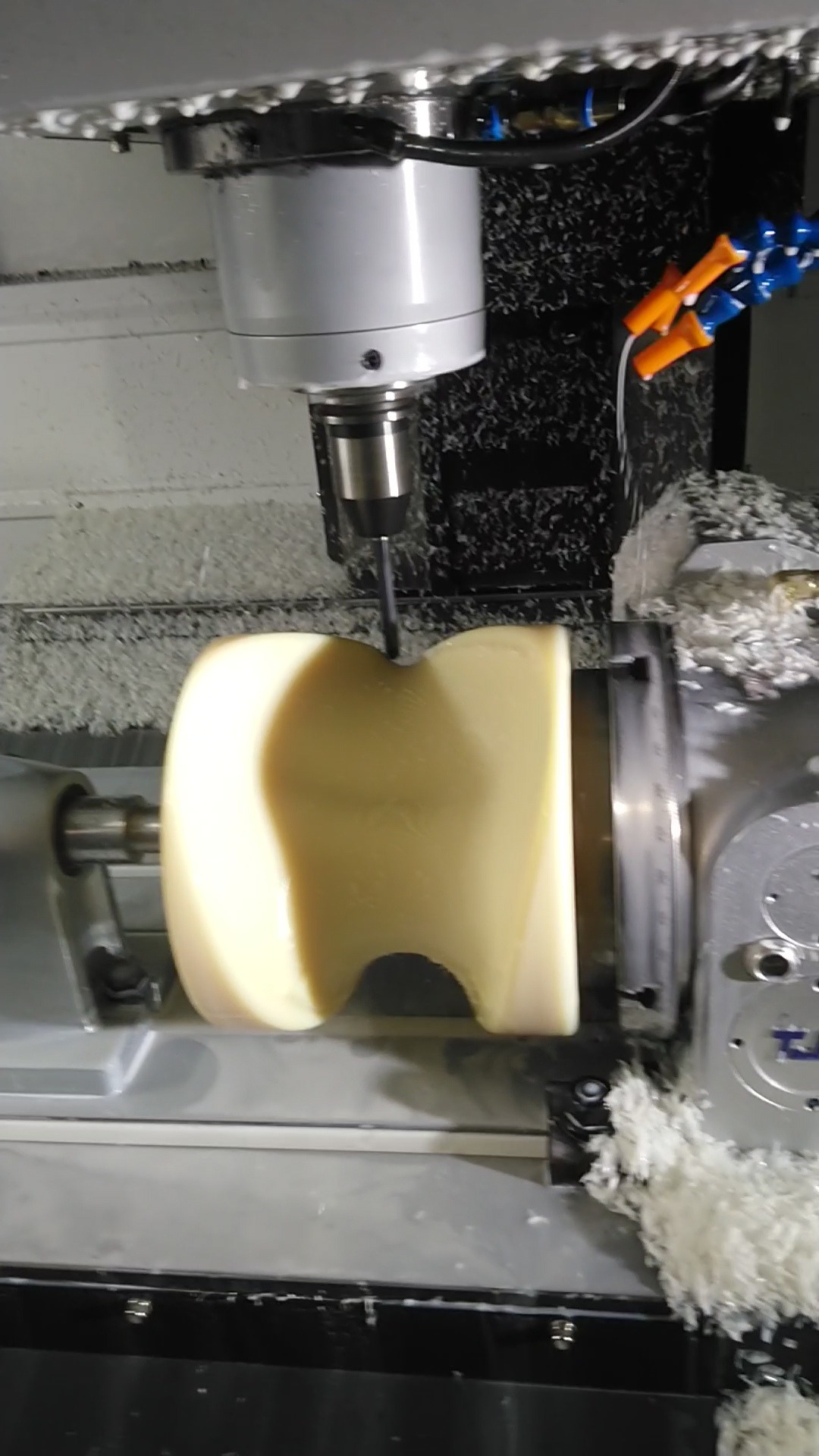Żółty element obrabiany na tokarce CNC. Wióry i płyn chłodzący w miejscu obróbki. Widoczny uchwyt tokarski i głowica z narzędziem.