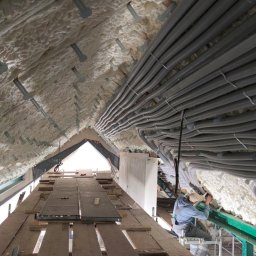 SANITARKA Marcin Skutnik - Izolacja poddasza pianą PUR i równolegle ułożone rury wentylacyjne, widok z rusztowania, pracownik w trakcie montażu,  szczegóły mocowania.