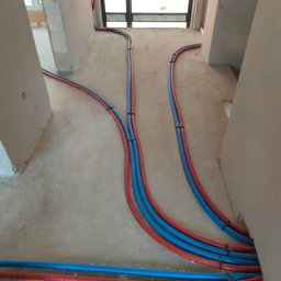 SANITARKA Marcin Skutnik - Instalacja ogrzewania podłogowego w trakcie montażu: rury w izolacji, prowadzone w surowym pomieszczeniu przed wylaniem posadzki, widoczne mocowania.