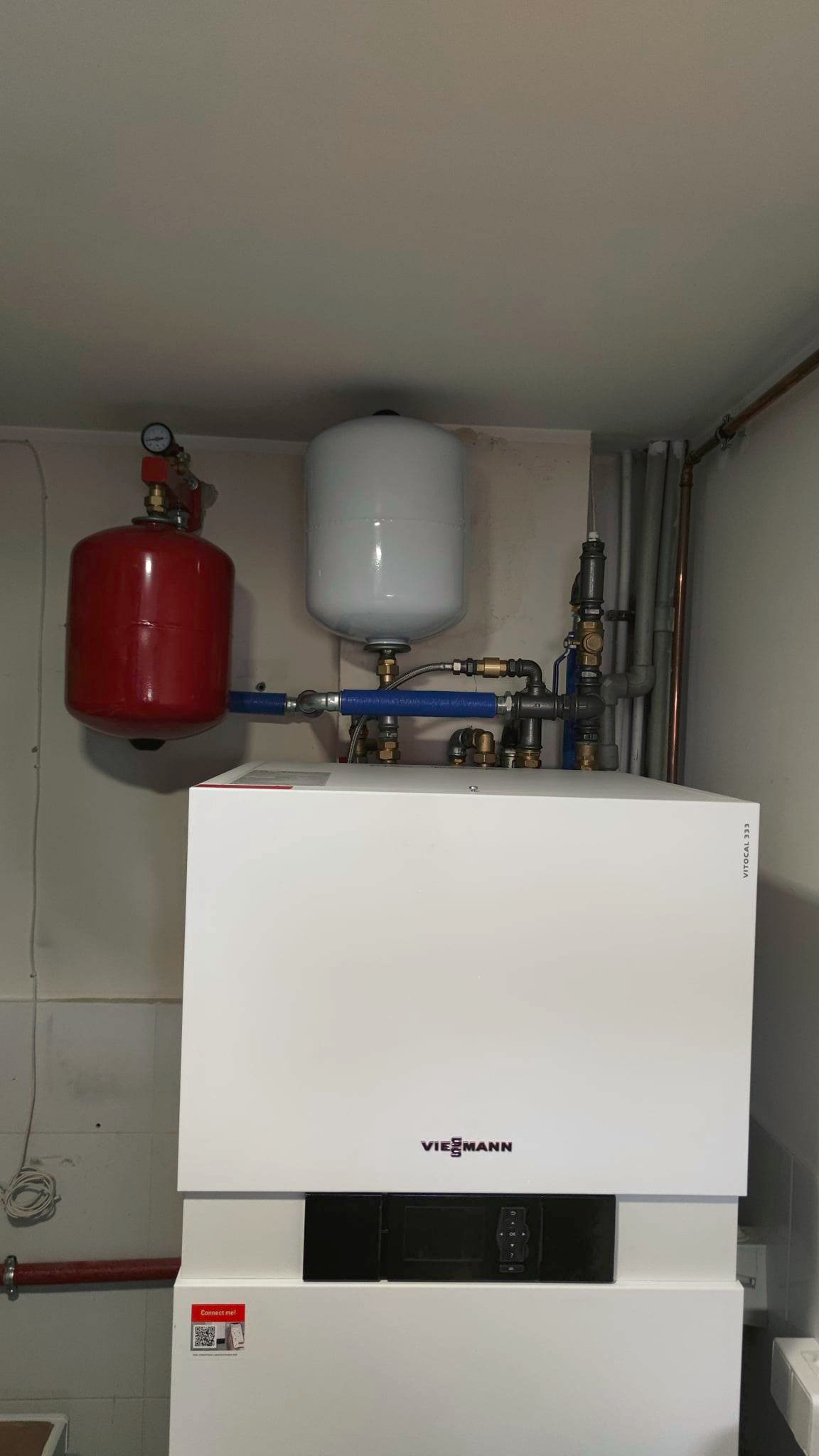 Nowoczesny, biały piec grzewczy Viessmann z czerwonym i szarym zbiornikiem wyrównawczym, rurami i armaturą. Instalacja grzewcza w pomieszczeniu.