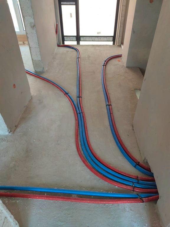 Instalacja ogrzewania podłogowego w trakcie montażu: rury w izolacji, prowadzone w surowym pomieszczeniu przed wylaniem posadzki, widoczne mocowania.