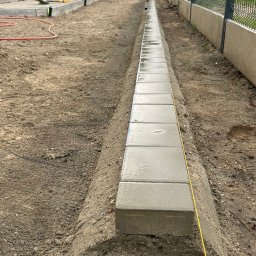 Jakub - Ułożony obrzeżnik z kostki betonowej wzdłuż ogrodzenia, wytyczony żółtym sznurkiem, na przygotowanym podłożu. Widoczne narzędzia i butelka wody w tle.