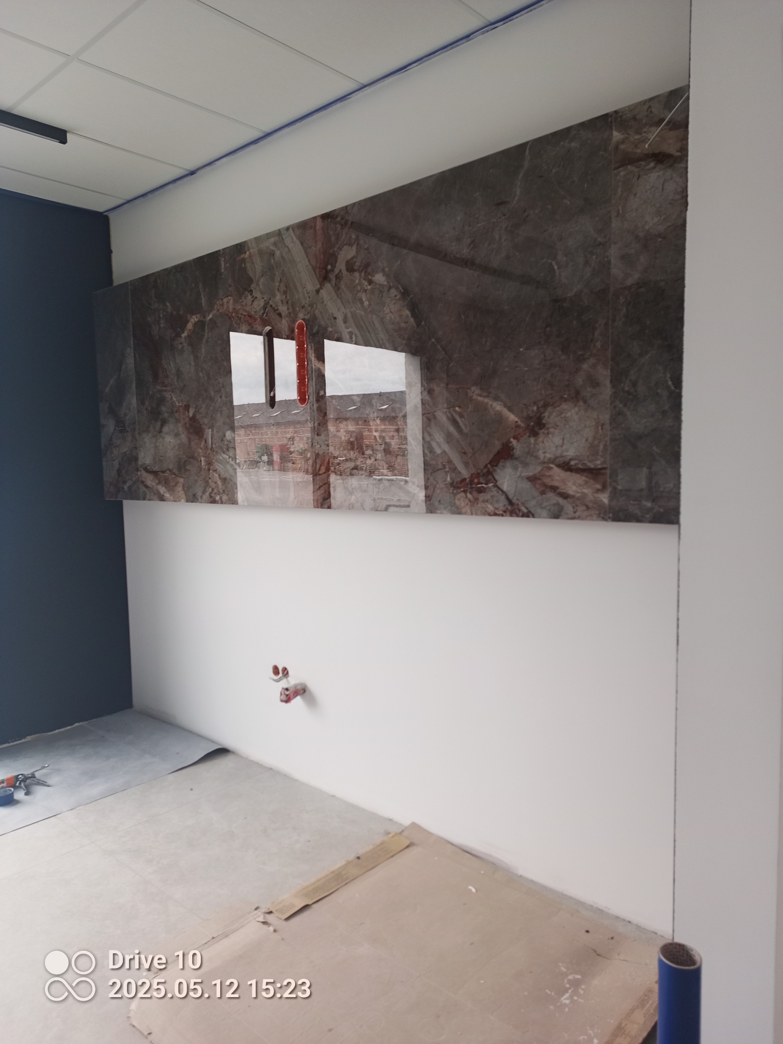 Łazienka w trakcie wykończenia: marmurowe płytki na ścianie nad białą lamperią, widoczne wyprowadzenia instalacji wodnej, surowa podłoga.