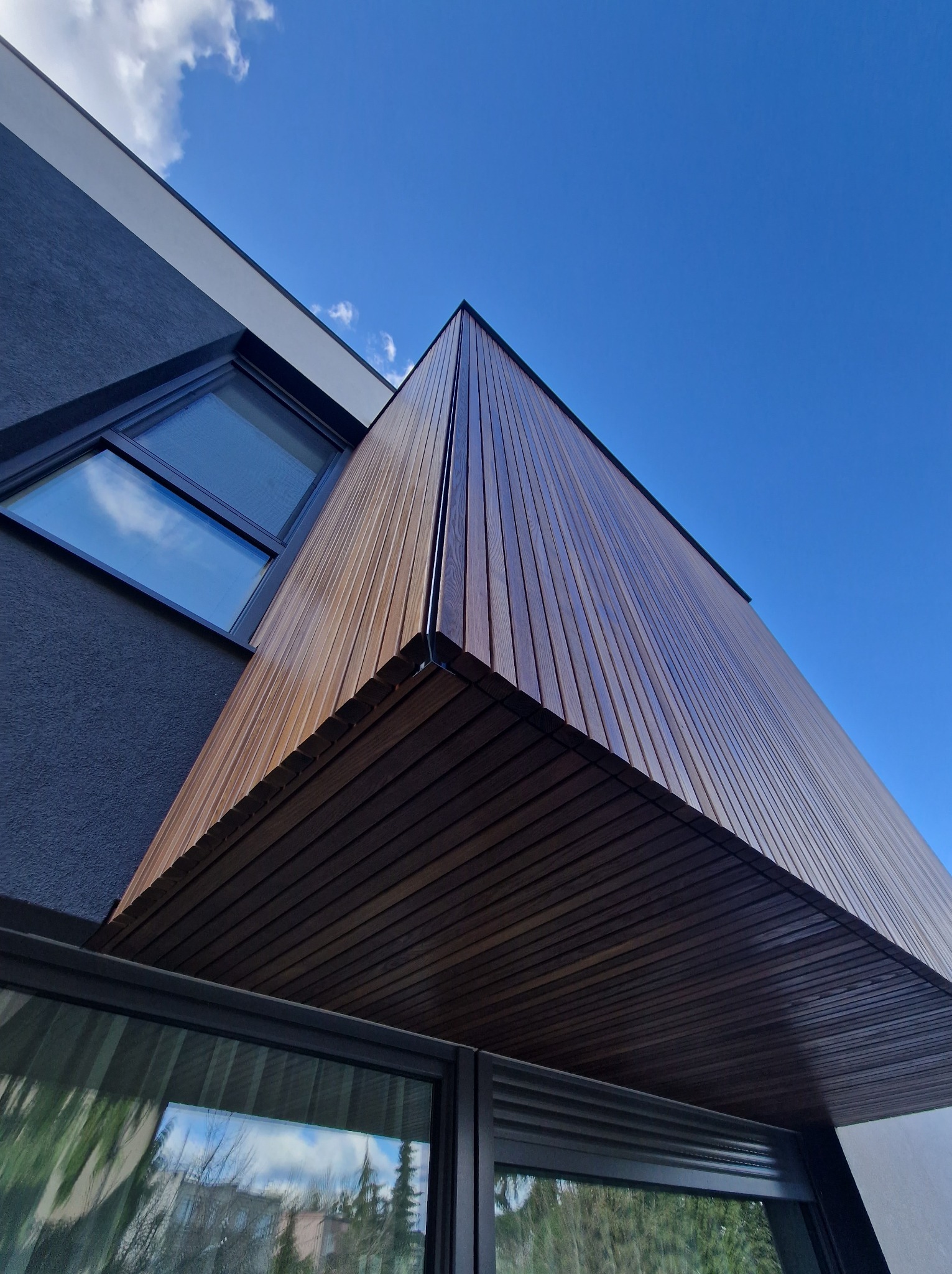 Nowoczesna elewacja budynku z pionowymi panelami z termojesionu 32x42 mm, widok z dołu na tle błękitnego nieba.