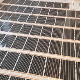 Rozłożone maty grzewcze na podłodze z widoczną siatką i folią termoizolacyjną, przygotowane do dalszych prac wykończeniowych. Widok z góry, ukośnie.