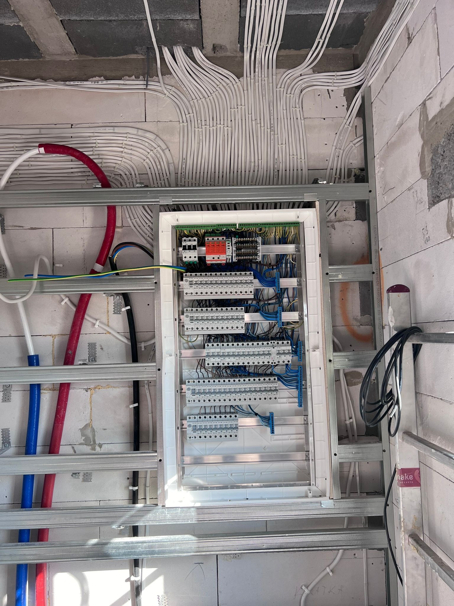 Rozdzielnica elektryczna z licznymi przewodami w budynku w trakcie budowy, widok z dołu, surowy stan, instalacje w ścianach.