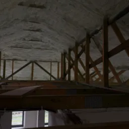 Poddasze z drewnianą konstrukcją i izolacją pianką PUR, widok z dołu na ocieploną połać dachową, fragment okna w tle.
