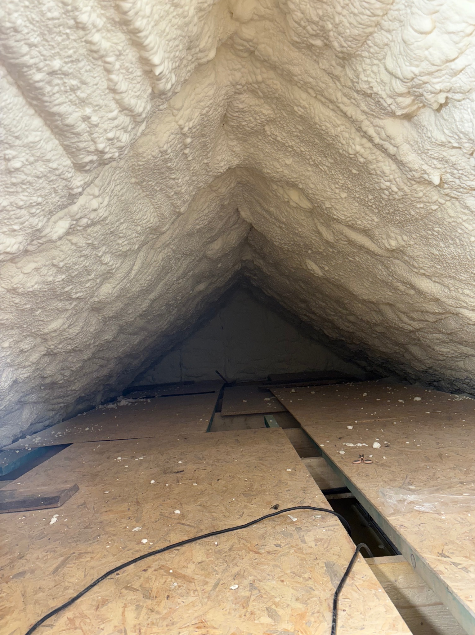 Poddasze po ociepleniu pianką PUR, widoczne płyty OSB na podłodze i równomierna warstwa izolacji na skośnych ścianach i suficie. Czarny kabel na podłodze.