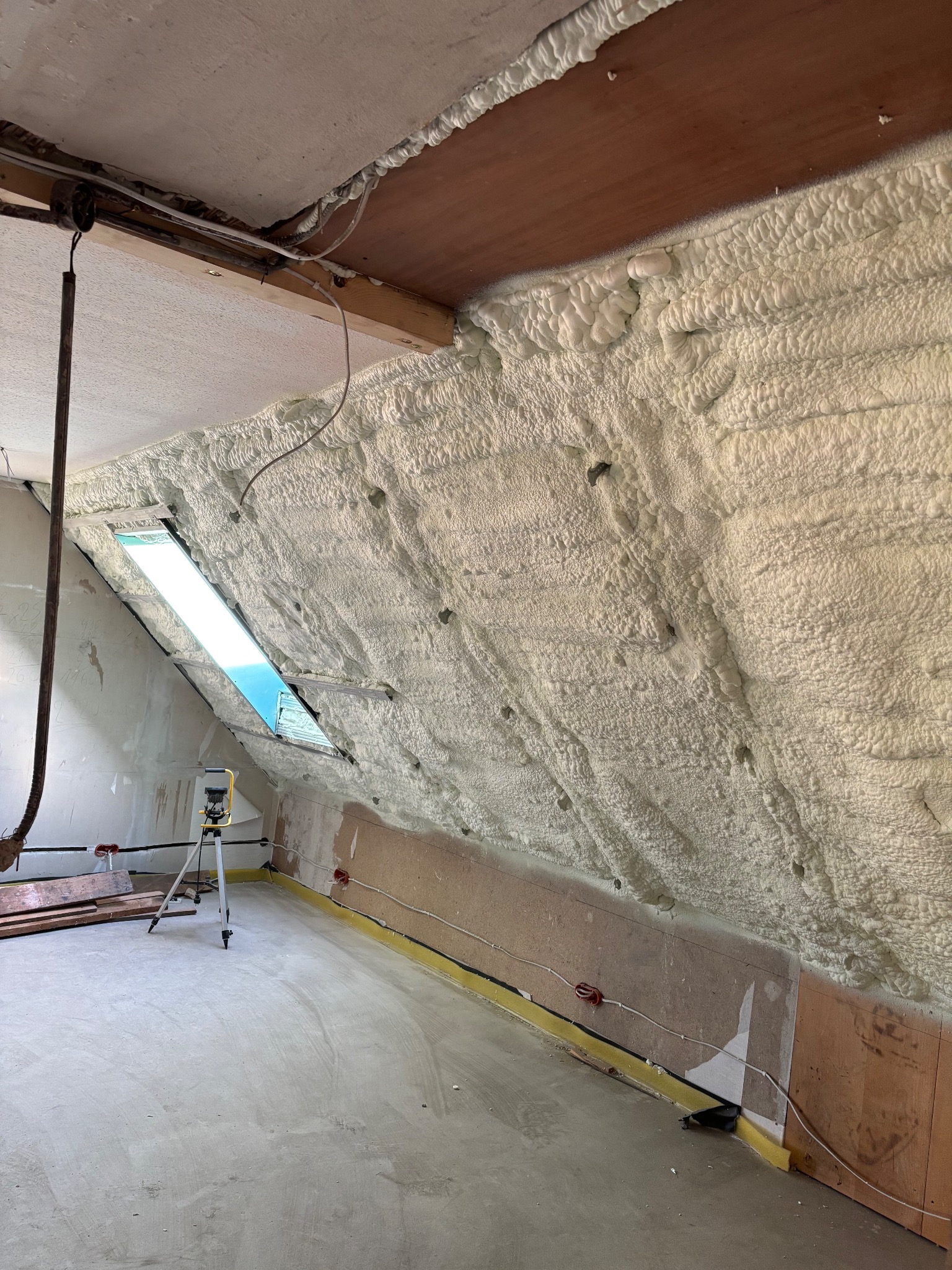 Poddasze po ociepleniu pianką PUR, widoczne okno dachowe, ściany pokryte grubą warstwą pianki, w tle sprzęt pomiarowy.