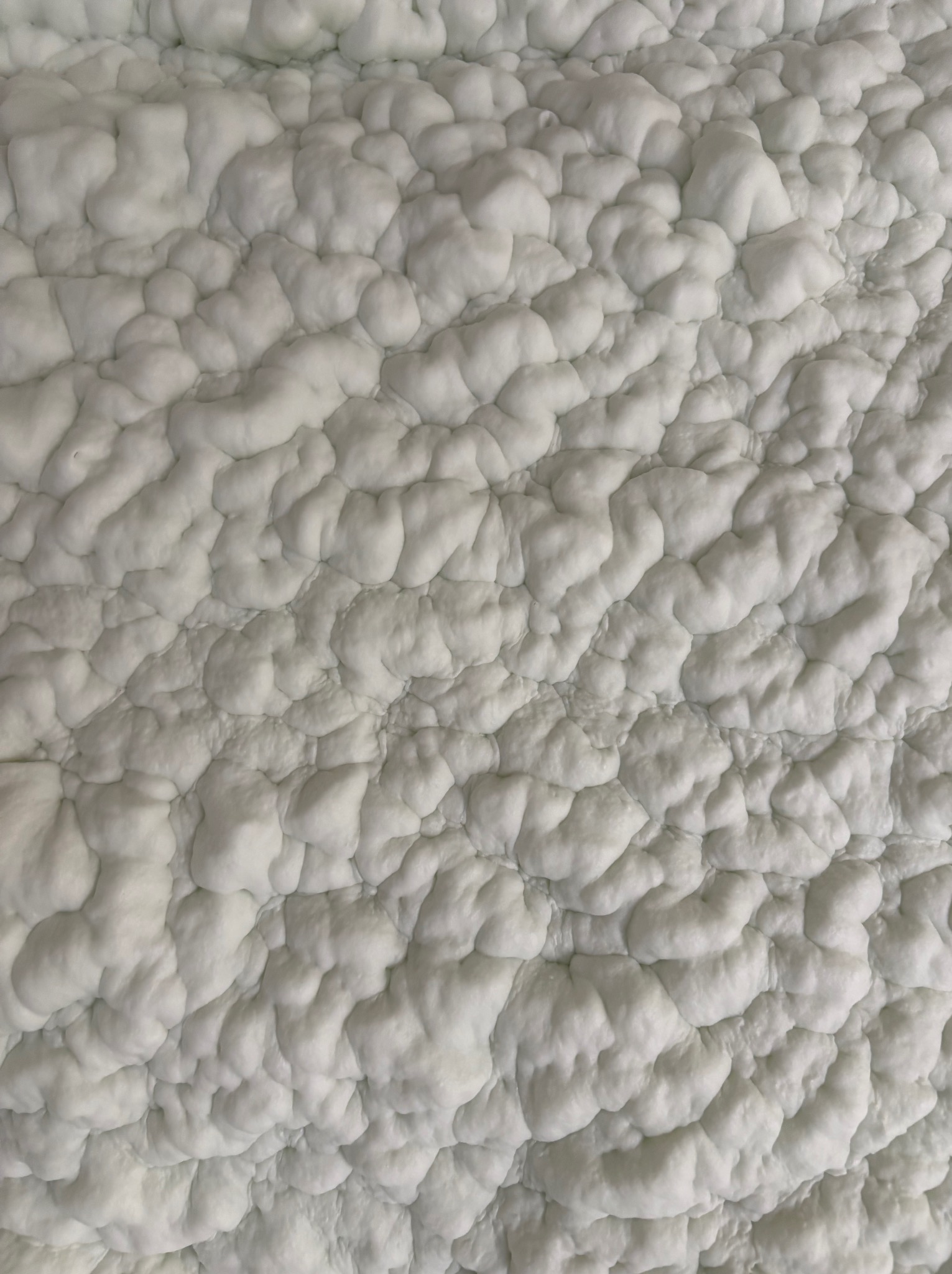 Szczegółowe ujęcie białej, nierównej powierzchni izolacji natryskowej PUR, ukazujące jej strukturę i gęstość na ścianie.