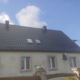 Dariusz Wieczorek - Dom jednorodzinny z nowym, ciemnoszarym dachem z dachówki ceramicznej, widoczne dwa okna dachowe, kominy i rusztowanie po prawej stronie.