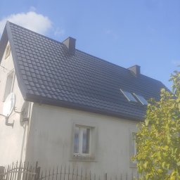 Dariusz Wieczorek - Dom jednorodzinny z nowym, ciemnoszarym dachem z dachówki ceramicznej, widoczne okna dachowe i komin, antena satelitarna na ścianie, metalowe ogrodzenie i drzewo z zielonymi liśćmi.