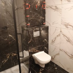 Dariusz Wieczorek - Nowoczesna łazienka w trakcie wykańczania: kabina prysznicowa z czarnymi profilami, wisząca toaleta i kombinacja płytek marmurowych w odcieniach bieli i czerni, z widocznymi klipsami poziomującymi...