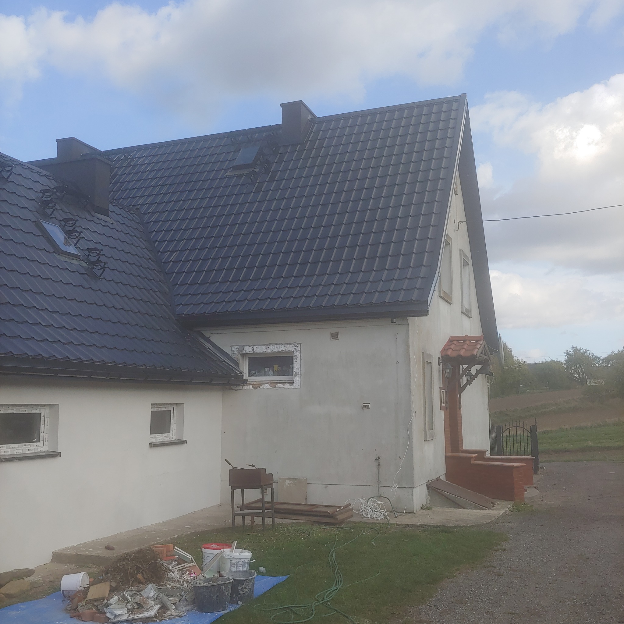 Dom jednorodzinny w trakcie remontu elewacji i wymiany okien, widoczne rusztowania, materiały budowlane i narzędzia na zewnątrz budynku.