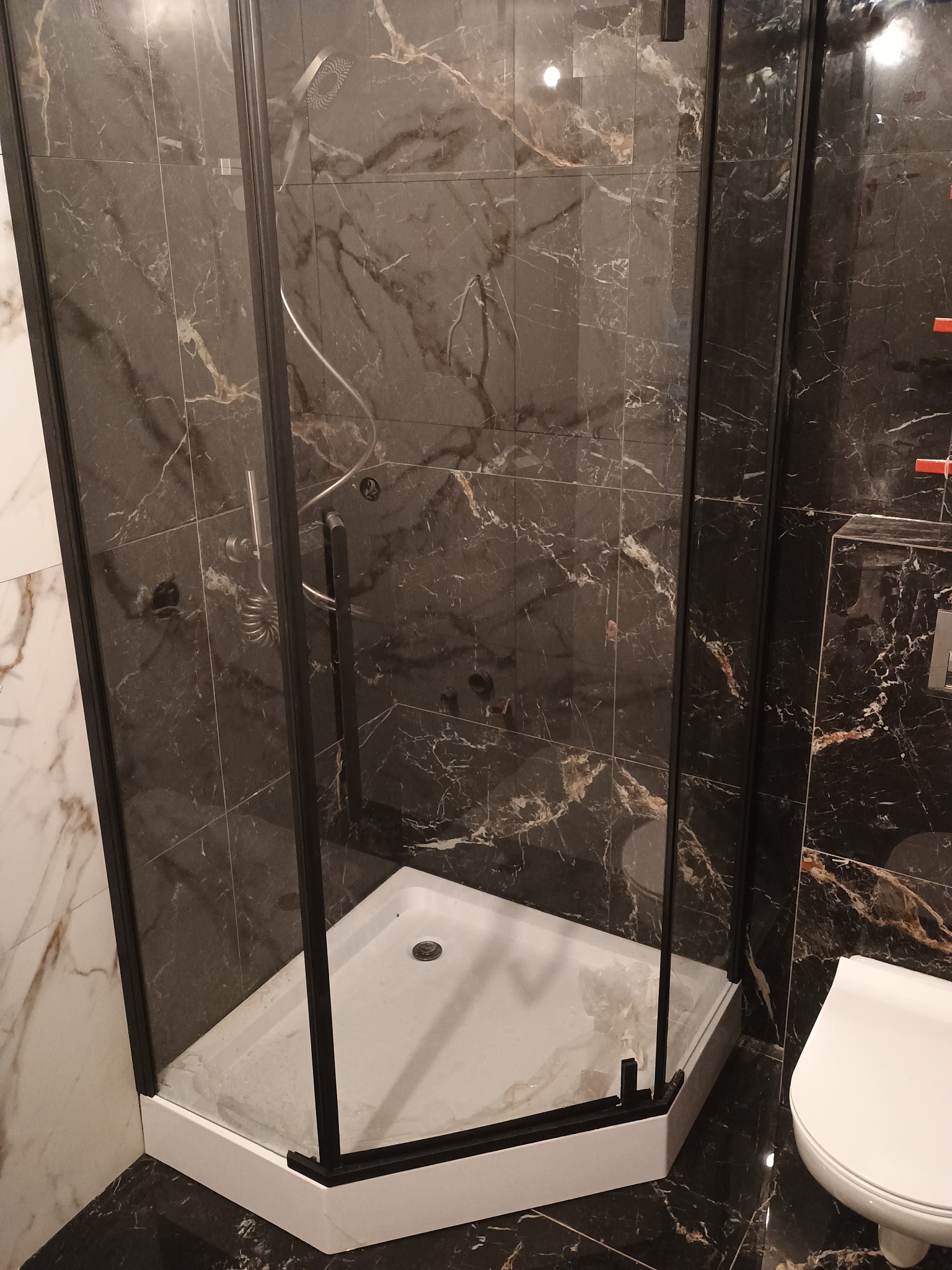 Nowoczesna kabina prysznicowa z czarną ramą i marmurowymi płytkami w łazience, widoczna biała toaleta.