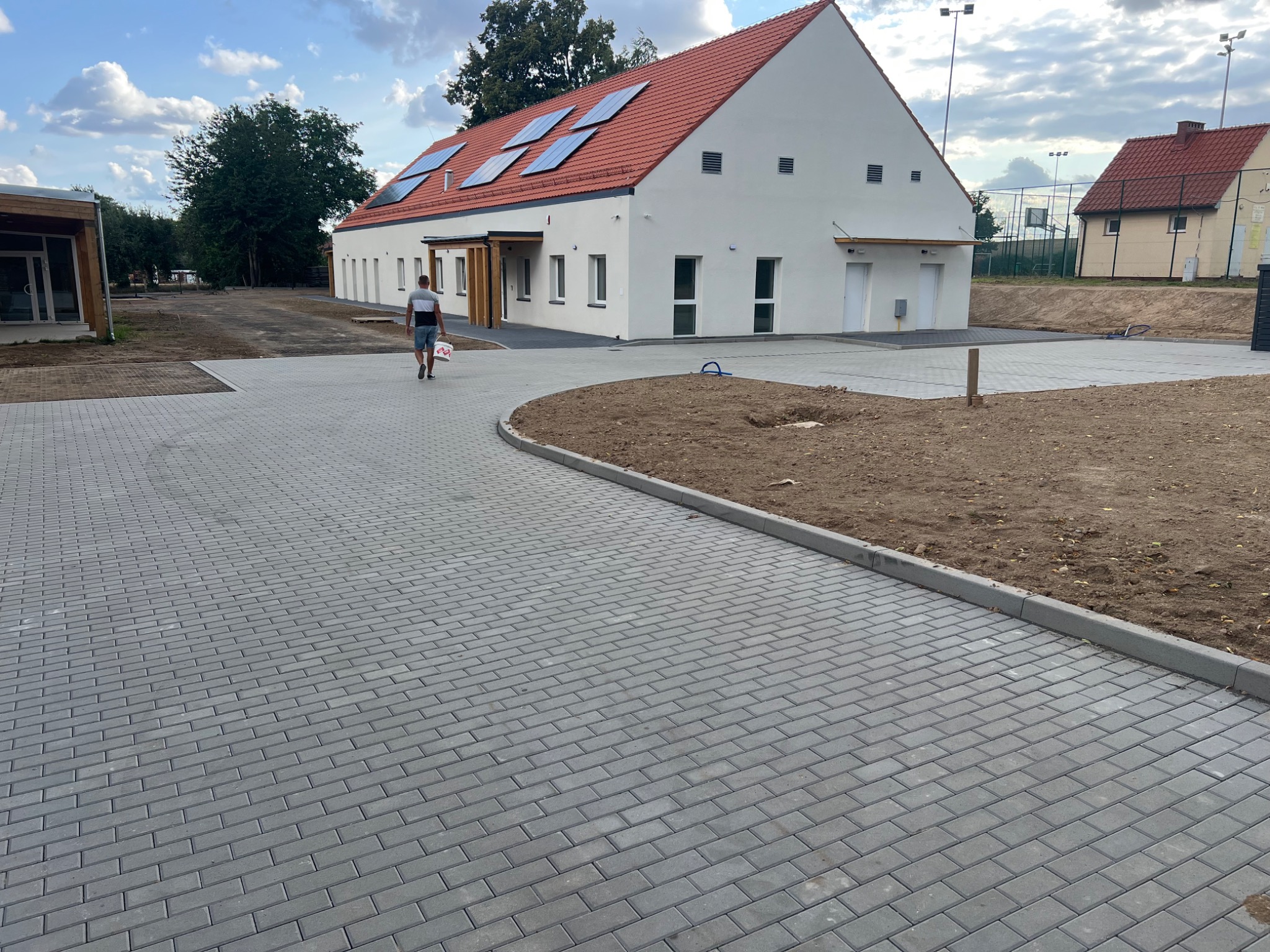 Nowa nawierzchnia z kostki brukowej w Legnicy, zarys budynku z panelami słonecznymi w tle. Widoczny fragment terenu przygotowanego pod nasadzenia.