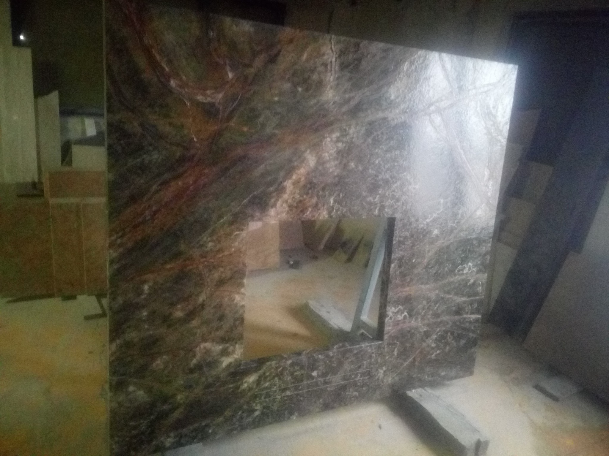 Częściowo obrobiony, brązowo-szary panel kamienny z otworem, prawdopodobnie element kominka, widoczny w surowym otoczeniu warsztatu.