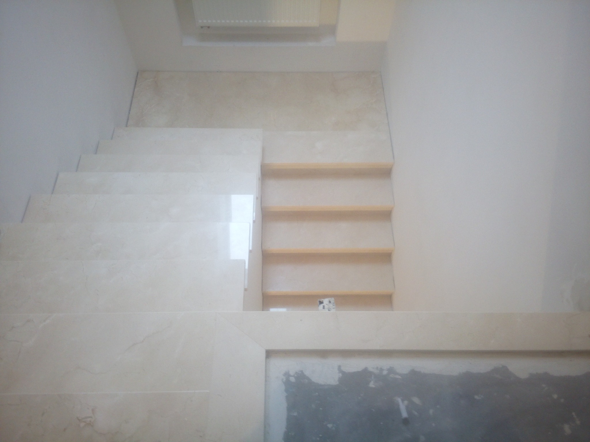 Wykończone schody z jasnego kamienia, widok z góry. Częściowo widoczne drewniane elementy konstrukcji schodów i fragment podłogi w trakcie prac wykończeniowych.