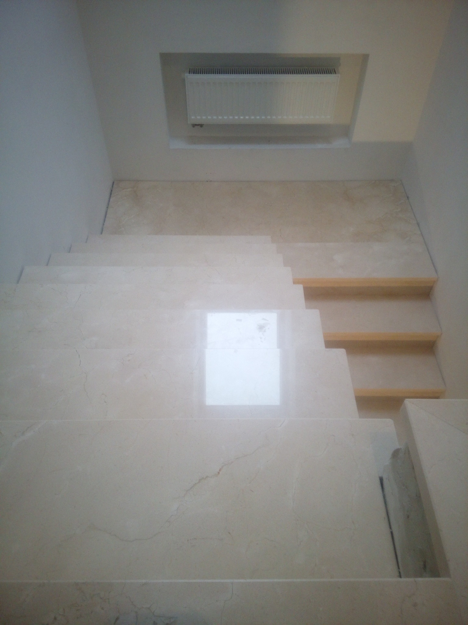 Wykończone marmurem schody wewnętrzne z widocznym grzejnikiem wnękowym, prezentujące elegancki detal wykończeniowy wnętrza.