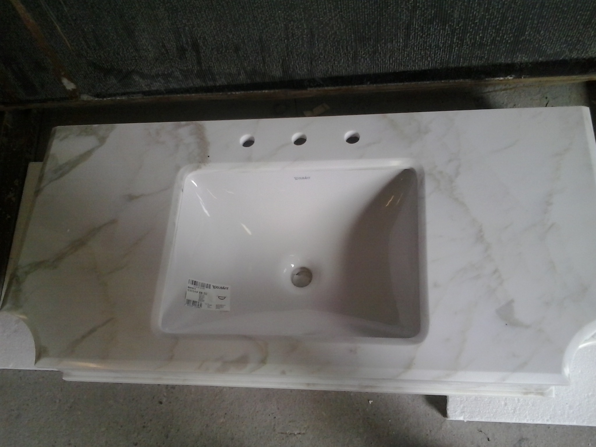 Marmurowy blat łazienkowy z umywalką Duravit, widoczne trzy otwory na baterię, leży na zabezpieczającym styropianie.