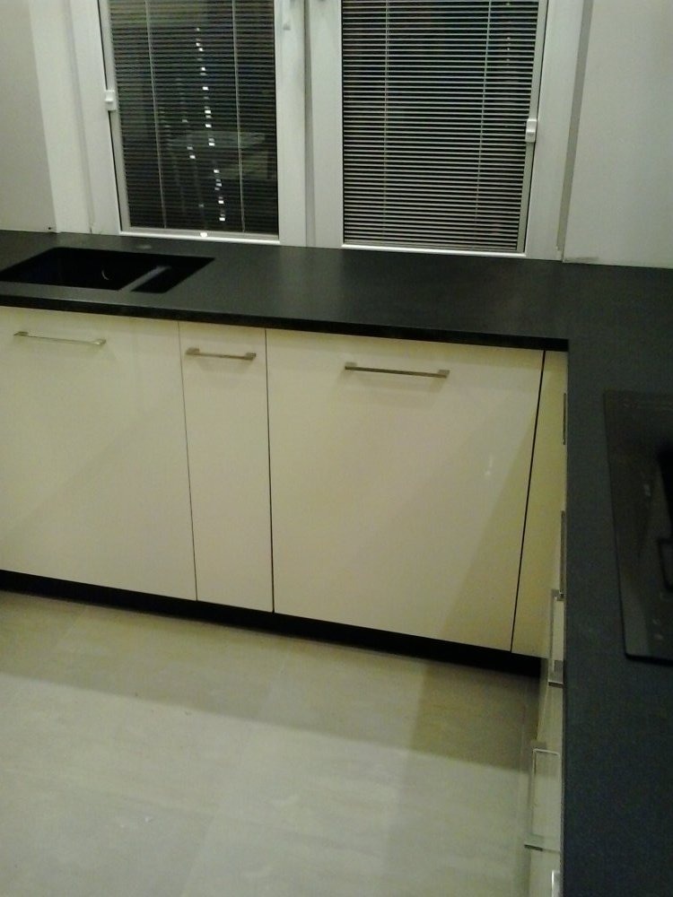 Kuchnia: beżowe szafki z czarnym blatem kamiennym pod oknem z żaluzjami. Minimalistyczny design, nowoczesne wykończenie. Widoczny zlew.