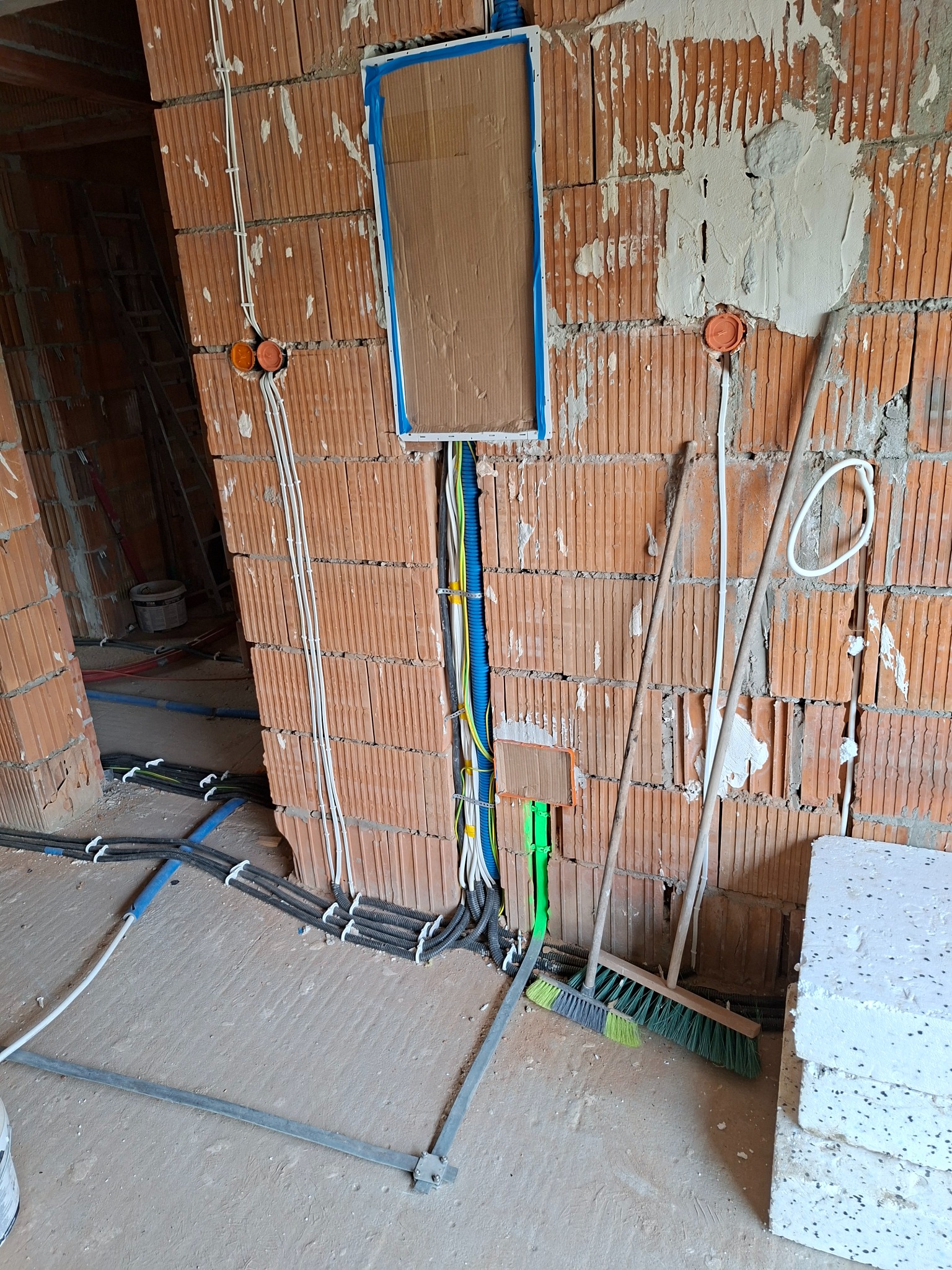 Instalacja elektryczna w surowym budynku: kable w peszlach prowadzone w ścianie z cegły, puszki instalacyjne, przewody w kolorach, przygotowane do dalszych prac wykończeniowych.