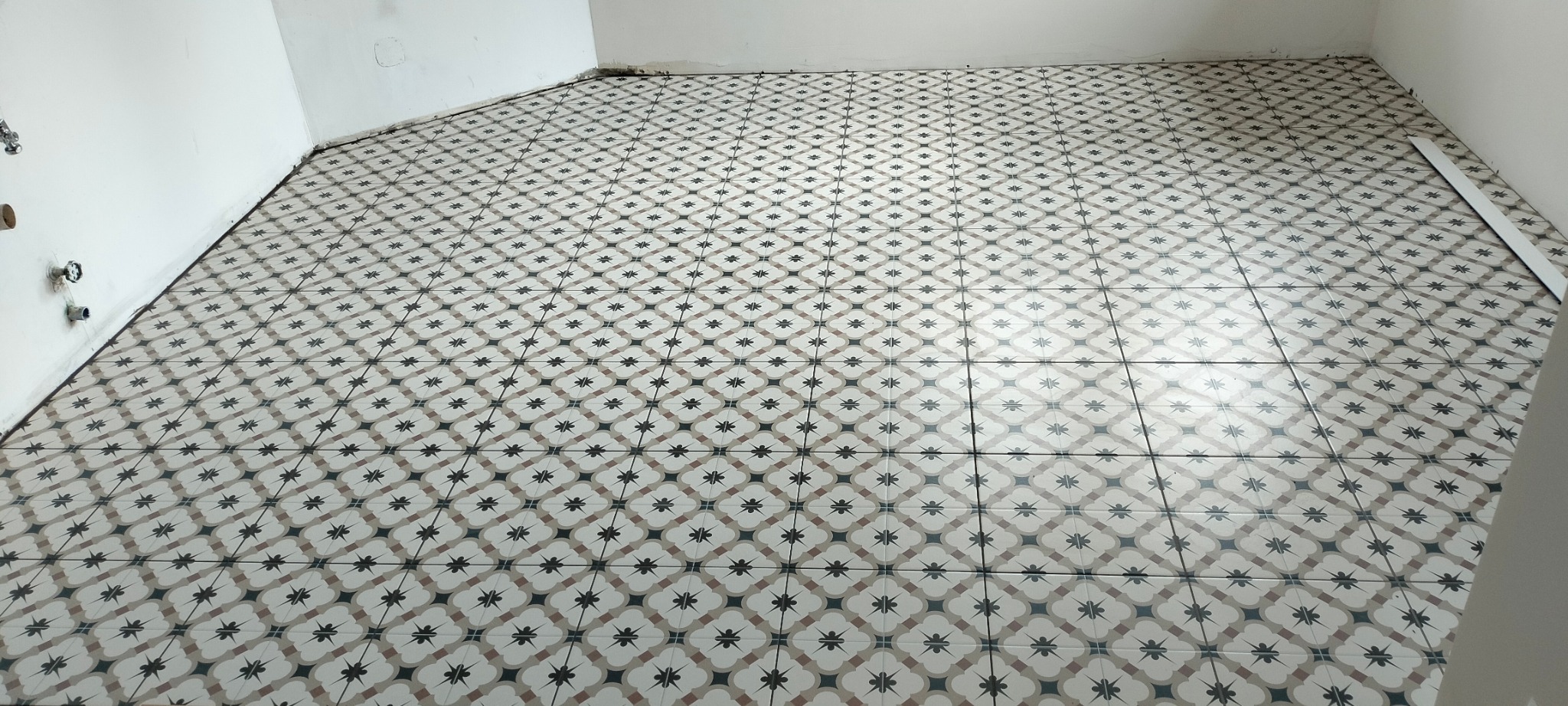 Ukończone układanie wzorzystych płytek podłogowych w pomieszczeniu w Krakowie, widoczne rury instalacji wodnej przy ścianie.